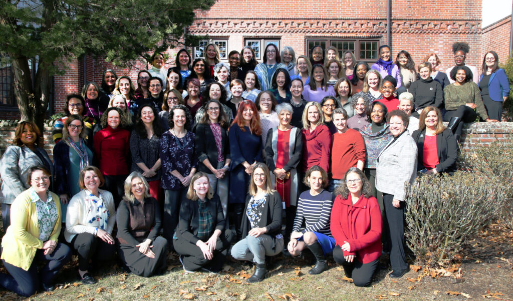 A group photo of the WHLI cohort of 68 women pictured outside a brick building with foliage surrounding